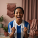 A diverse woman, 30s, smiling joyfully and looking excited, as if cheering for a soccer game.